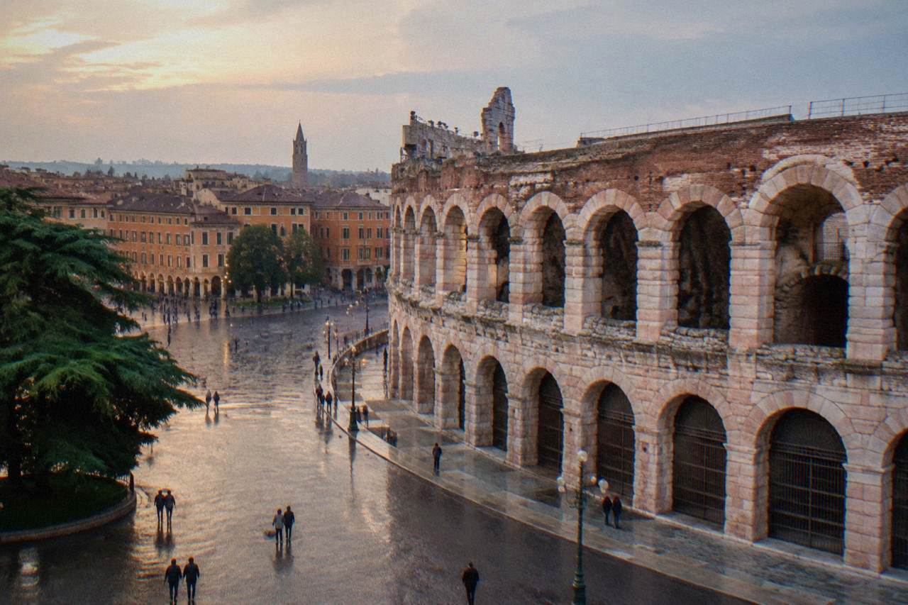 The pink stone arches of the Arena di Verona rising above Piazza Bra in evening light