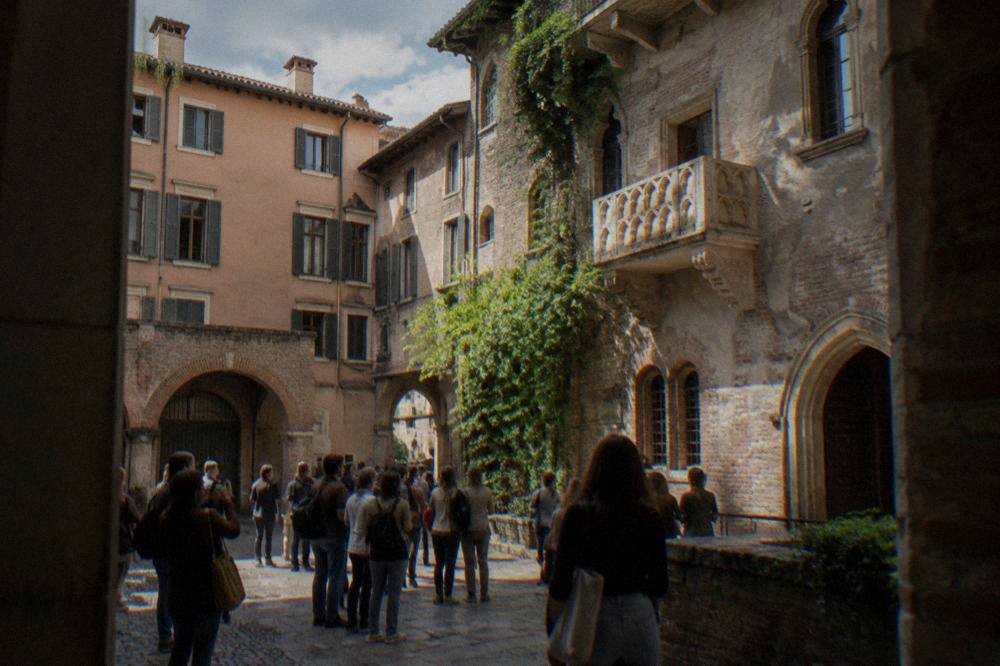 Visitors gathered in a small brick courtyard beneath a stone balcony in Verona