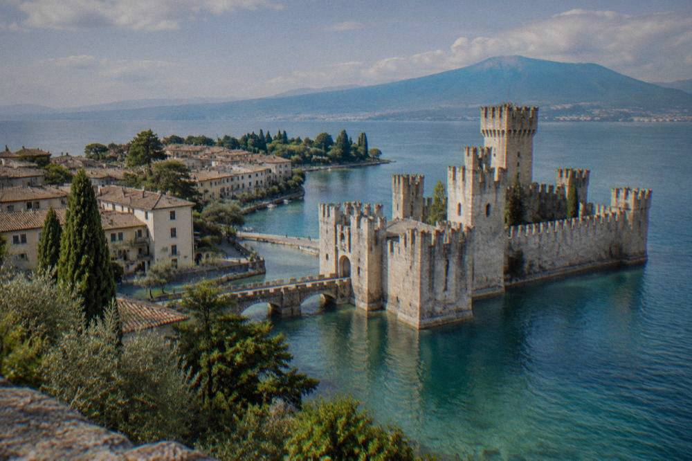 The walled peninsula of Sirmione reaching into Lake Garda, with a stone castle tower at the water's edge and hills behind