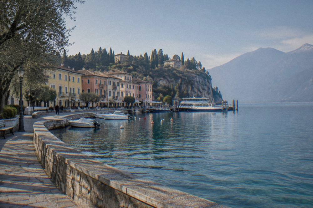 Pastel lakeside buildings along the shore of Lake Garda with ferry boats moored at a small pier