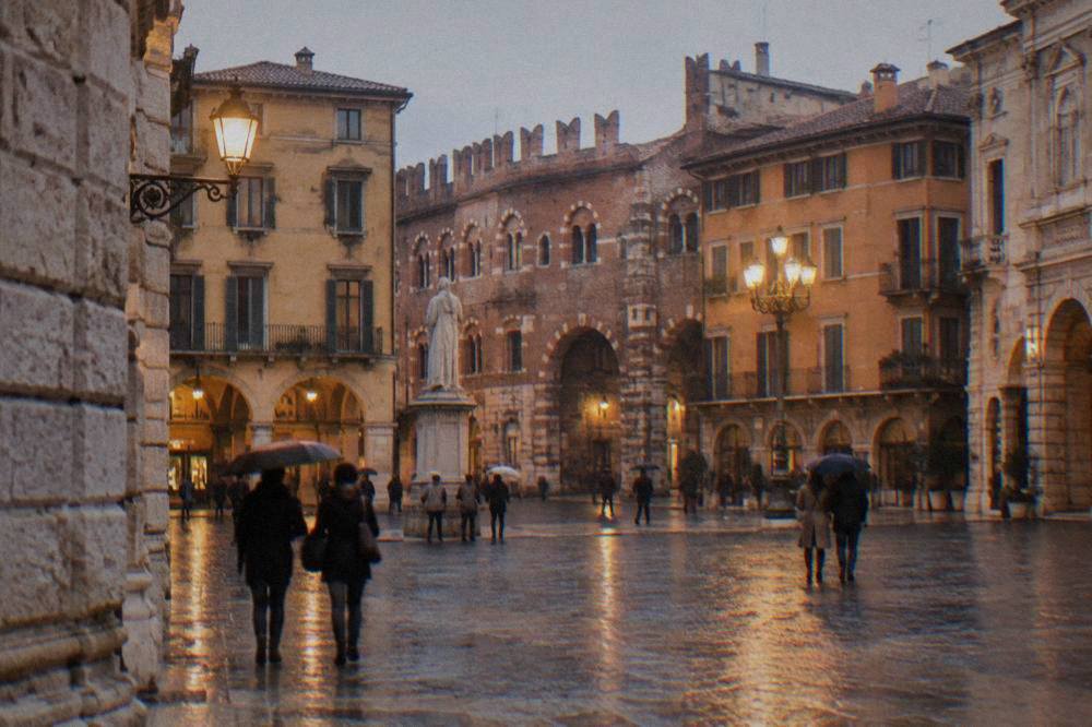 People walking across a lamplit square in Verona in the evening with historic buildings around it