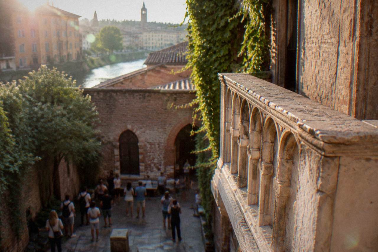 A stone balcony above a brick courtyard in Verona with tourists gathered below