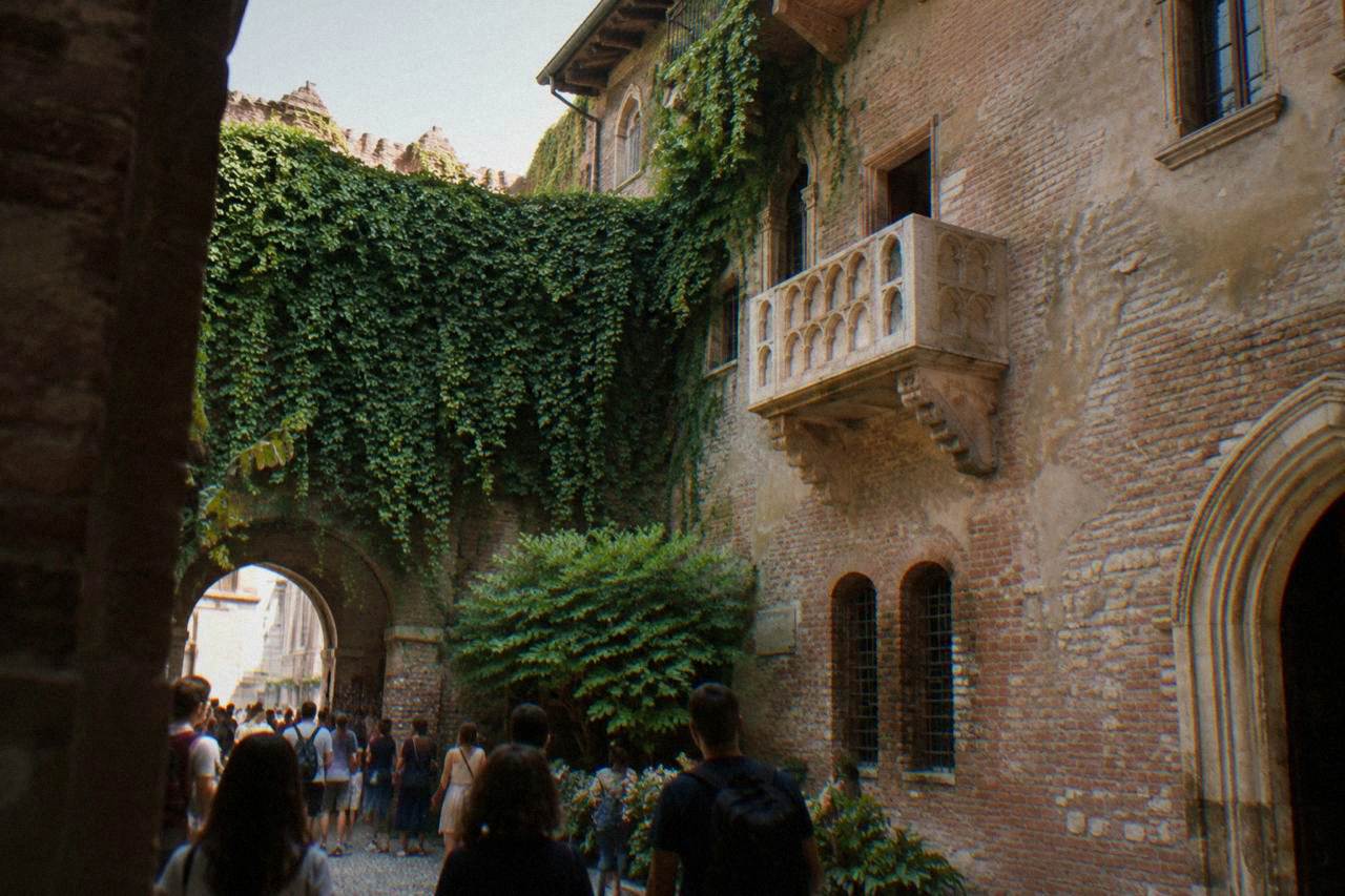 The stone balcony above the small courtyard of Juliet's House in Verona, with brick walls and visitors below