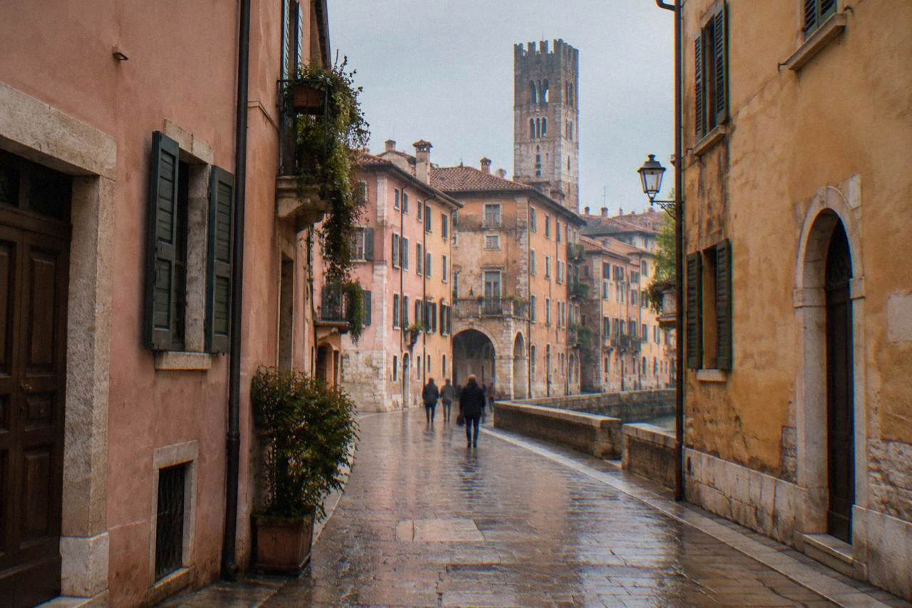 A quiet Verona street of rose-pink buildings with a stone tower rising above the rooftops