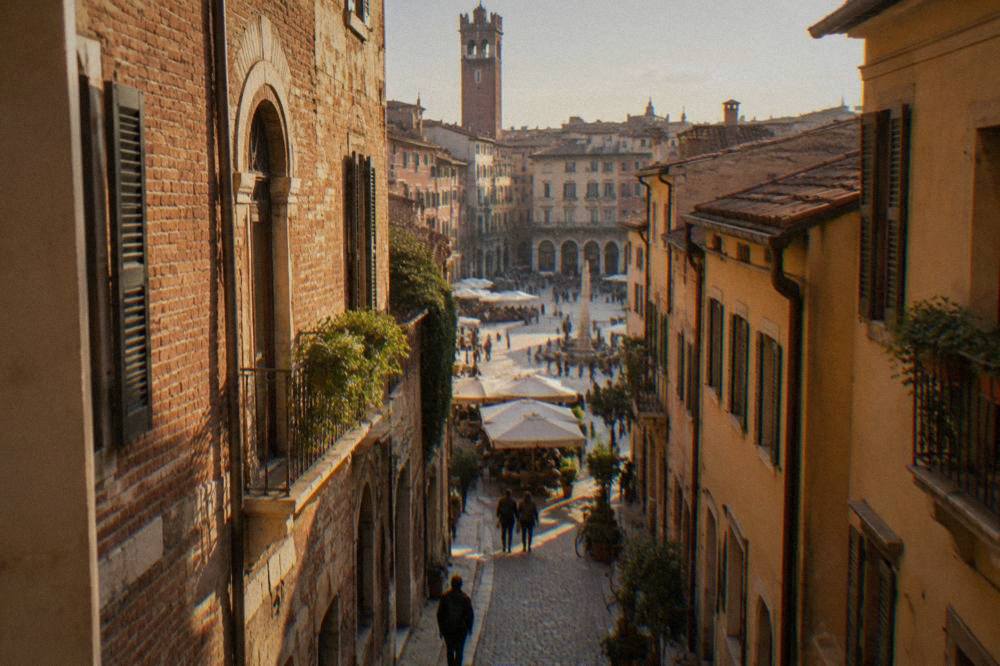 A narrow cobbled Verona street with warm brick facades leading toward Piazza delle Erbe