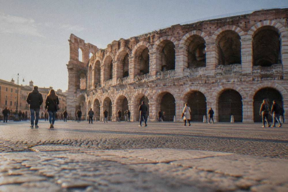 The rose-pink Arena of Verona seen from Piazza Bra with people crossing the open square on foot