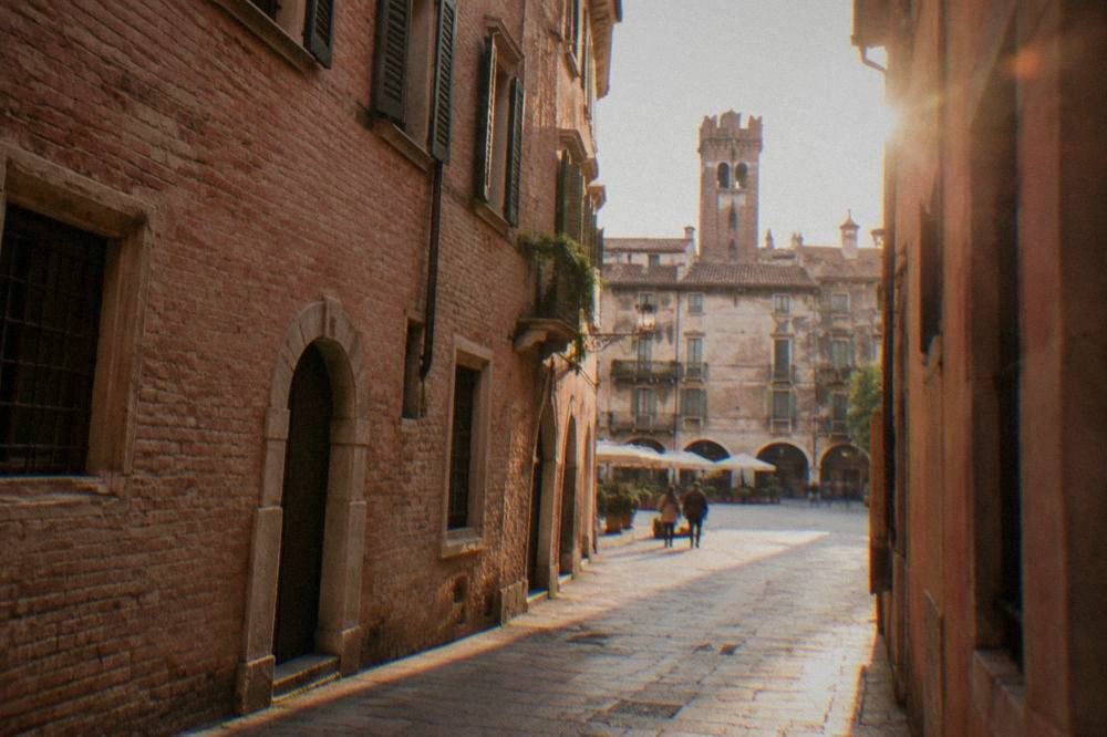 A narrow medieval Verona street with pink brick facades opening toward a sunlit piazza