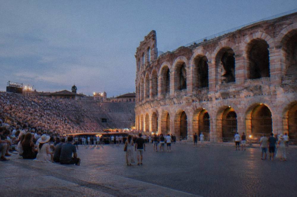 An evening crowd in casual summer clothing seated on the stone steps of the Verona Arena before an outdoor performance