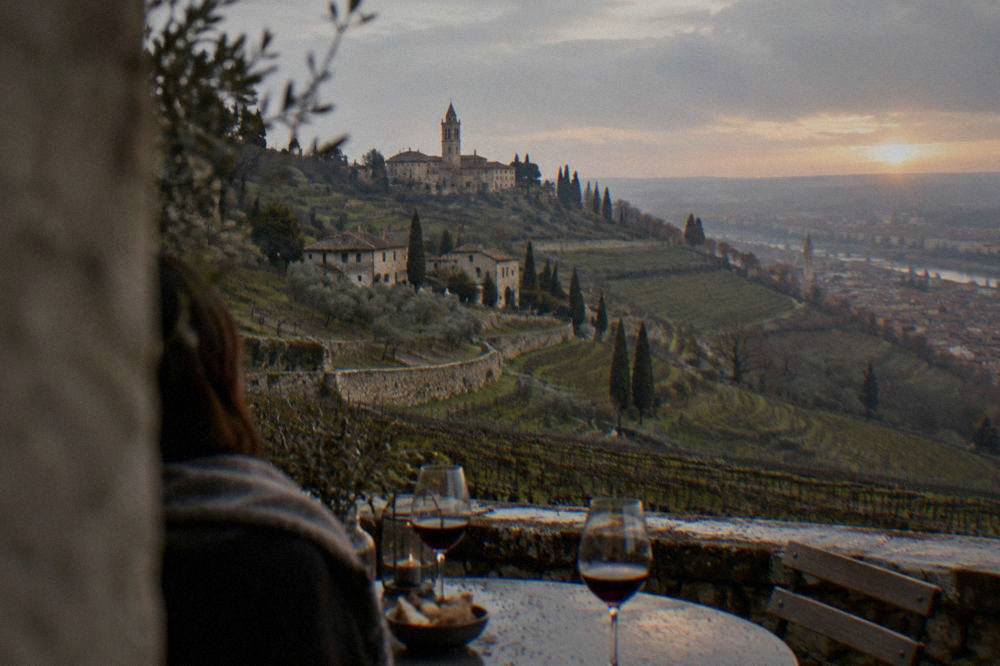 A table set with glasses of red Valpolicella wine overlooking Verona rooftops at sunset