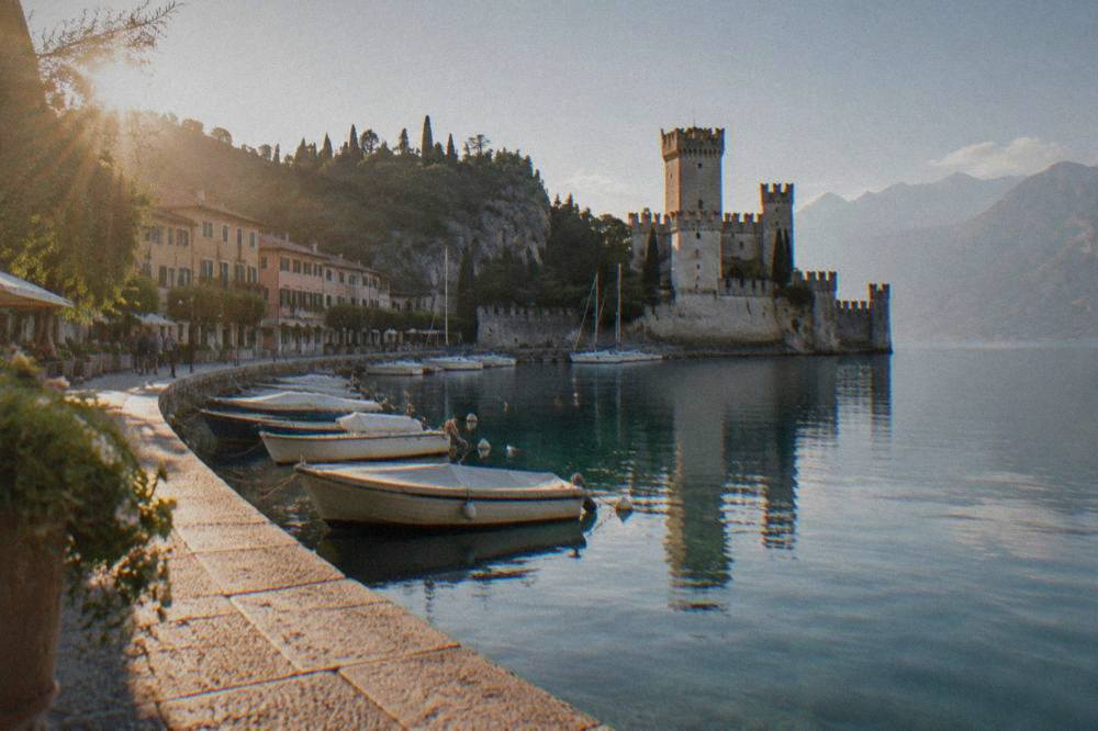 A historic lakeside castle reflected in calm water with boats moored alongside