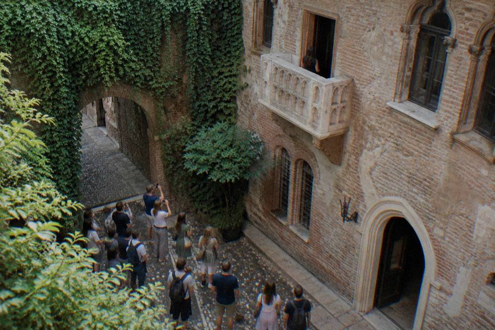 Visitors gathered in a narrow medieval courtyard looking up at an old stone balcony
