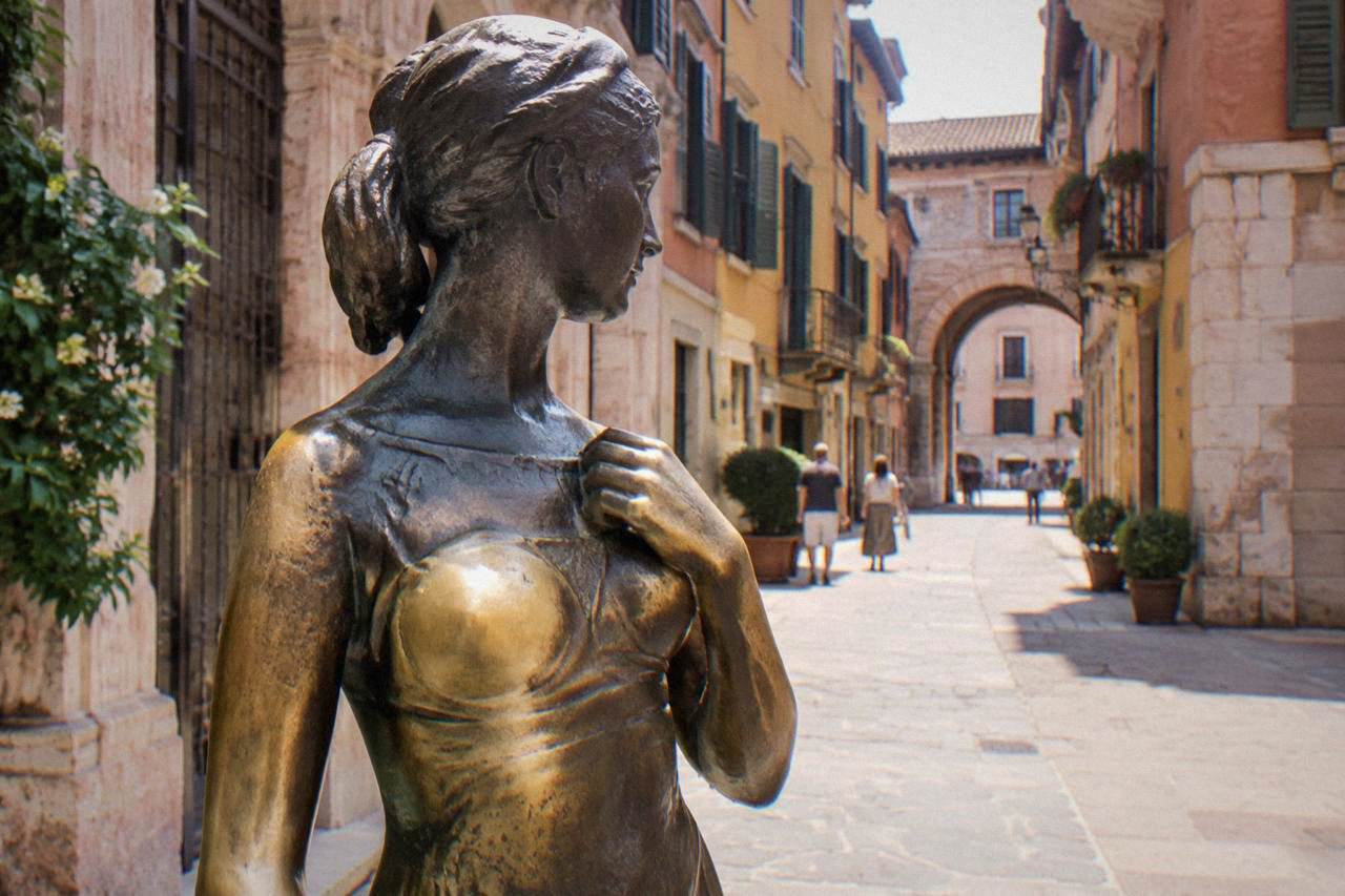 A bronze statue of Juliet standing in a stone courtyard in Verona, its polished surface catching the light