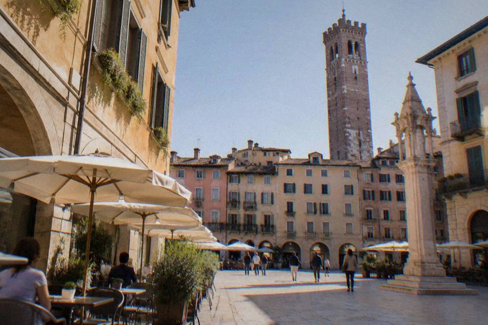 A sunlit square in northern Verona with cafe tables and morning shoppers