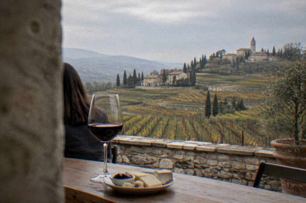 A glass of red Amarone wine on a wooden counter beside a plate of local cheese