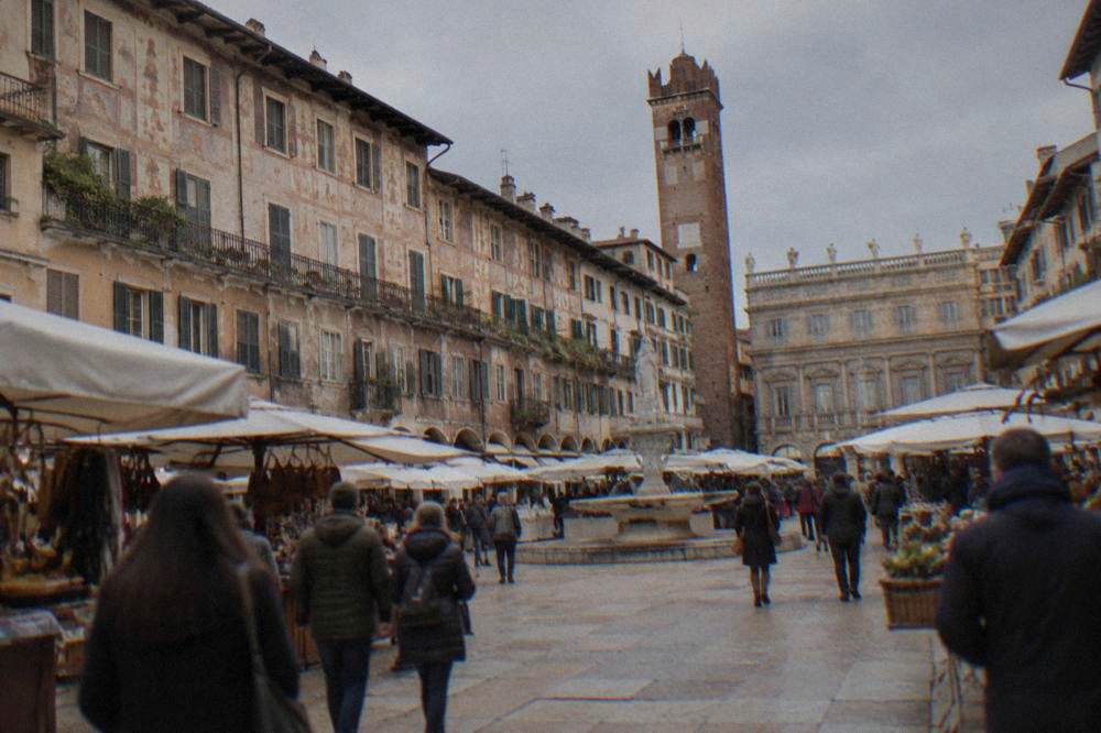 Crowded market square with awnings and historic frescoed buildings in Piazza delle Erbe