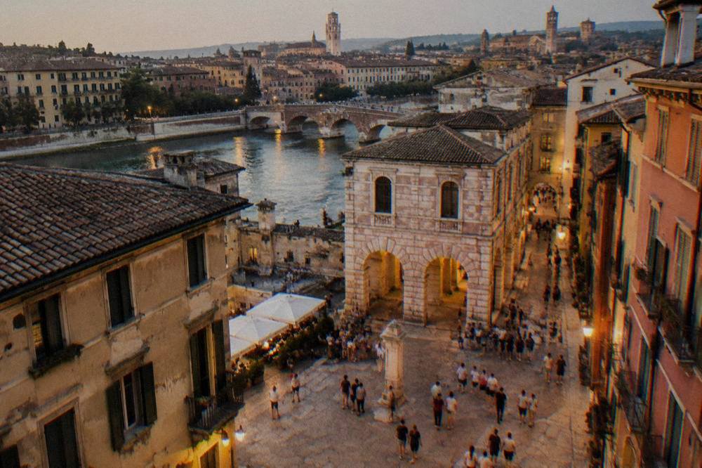 Evening view of a lit piazza in Verona with people walking between old buildings