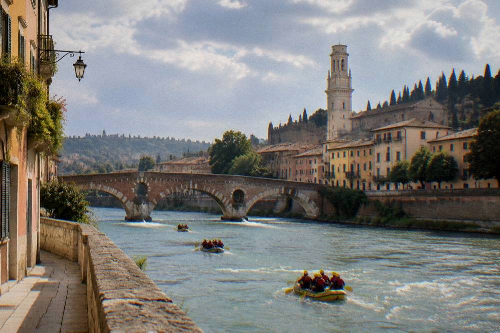 People rafting on the Adige river past old city walls and bridges