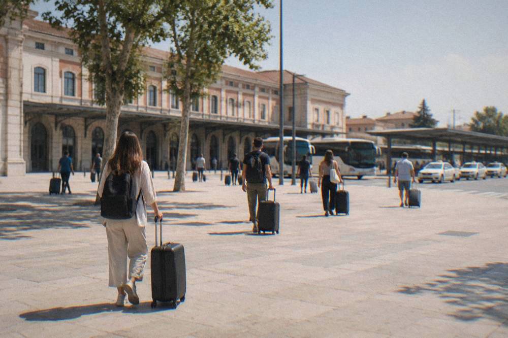 Travellers with suitcases crossing the open square in front of Verona Porta Nuova station on a bright morning
