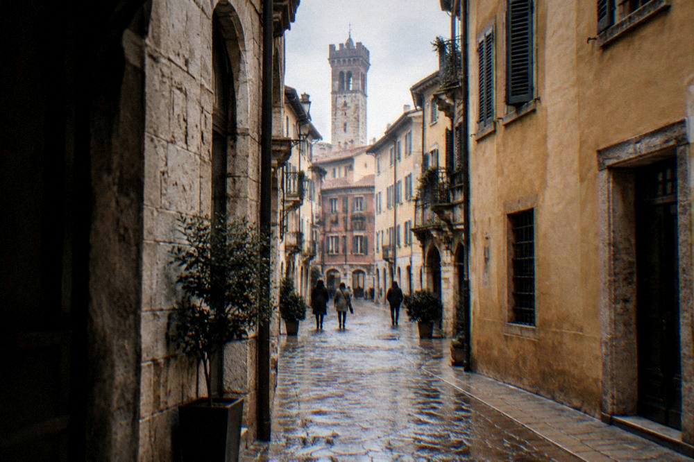 A narrow medieval lane in central Verona with stone buildings and a distant tower
