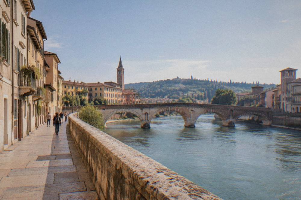 The Adige river in Verona flowing under an old stone bridge with hills in the distance