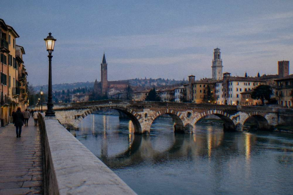An old stone bridge over the Adige river in Verona with the city skyline behind