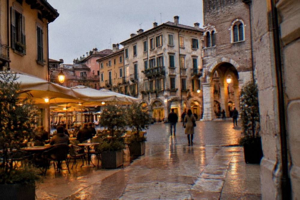A small neighborhood square in Verona at dusk with cafe tables under warm lights