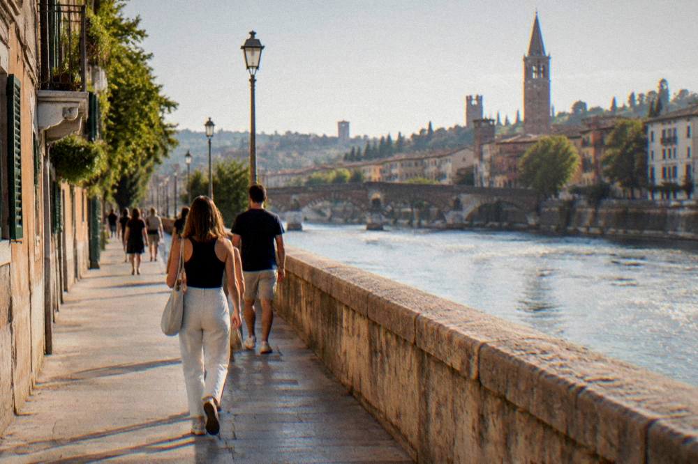 People walking along a riverside path beside the Adige in Verona in late afternoon light