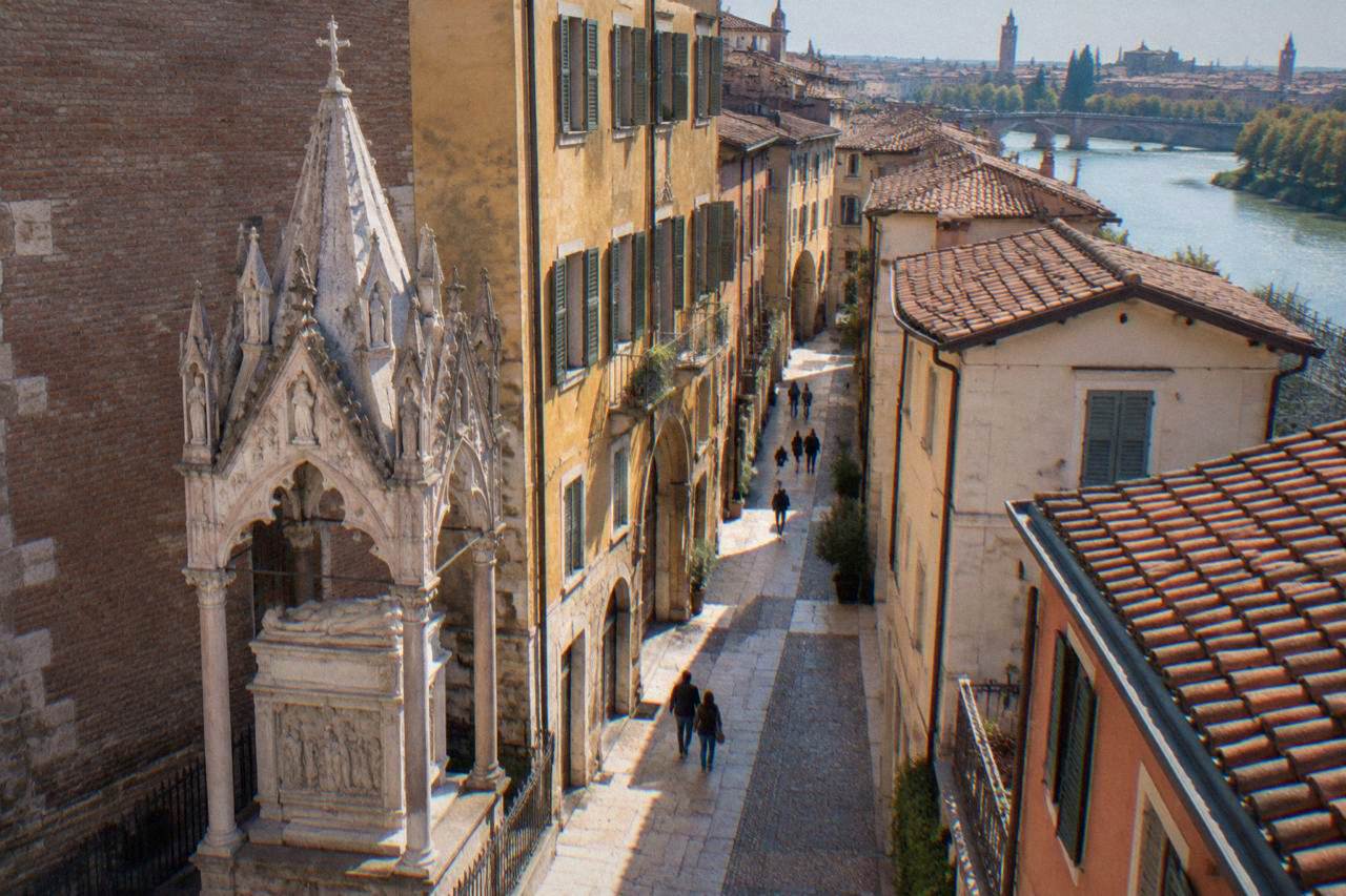 Gothic stone tomb monument with a pointed canopy beside a narrow brick street in Verona