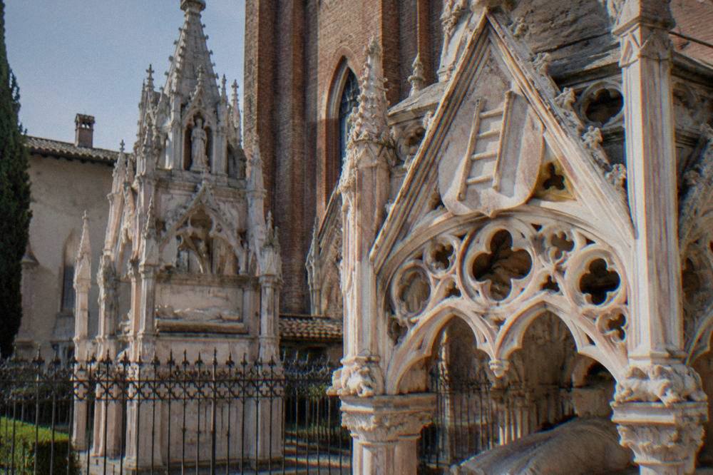 Close view of a carved stone tomb canopy with a ladder emblem and openwork Gothic tracery