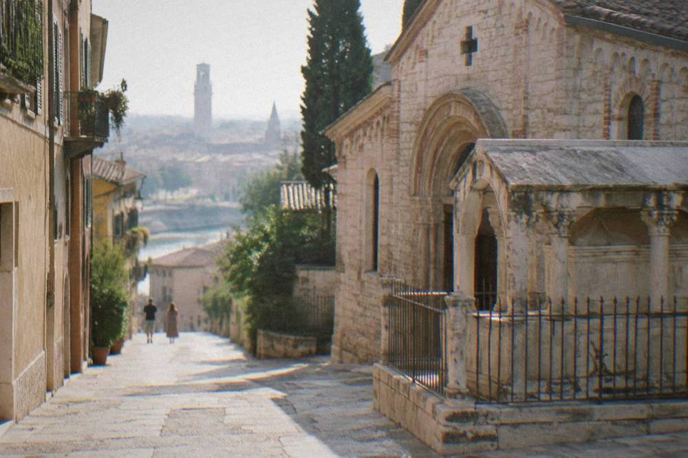Narrow medieval street in Verona with a stone tomb enclosure beside a small Romanesque church facade