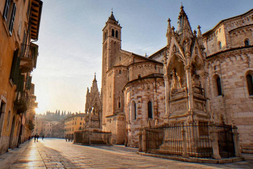 Wide view of a quiet Verona street with Gothic tomb monuments beside a Romanesque church at golden hour