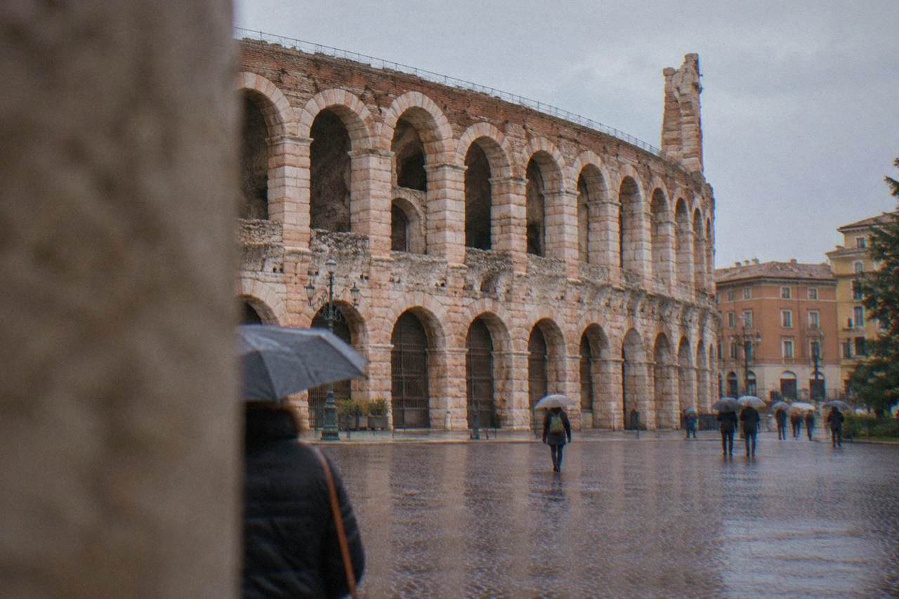 The pink stone facade and arched wing of the Arena di Verona rising above Piazza Bra