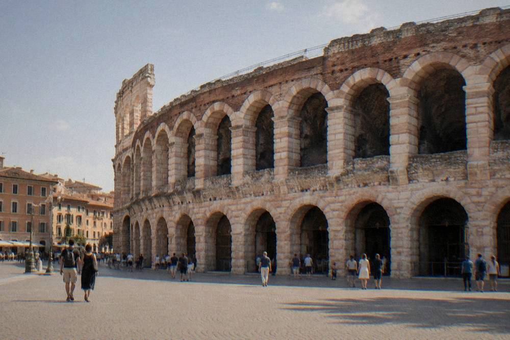 Visitors walking through the ground-level arcade of the Arena beneath stone arches