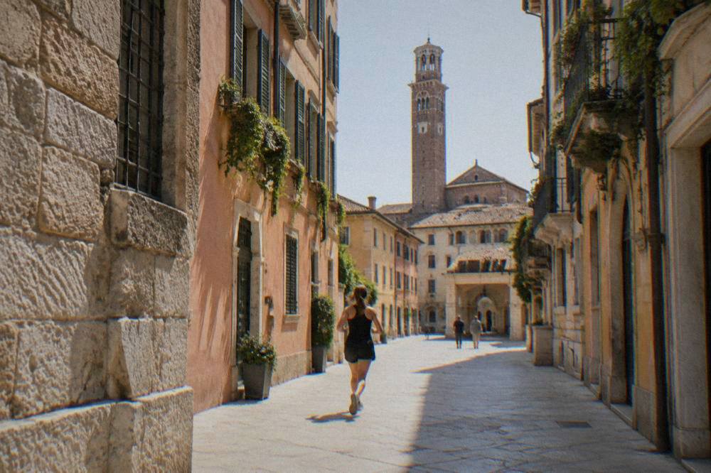A tall Romanesque bell tower rising beside a church roofline in Verona under a clear sky