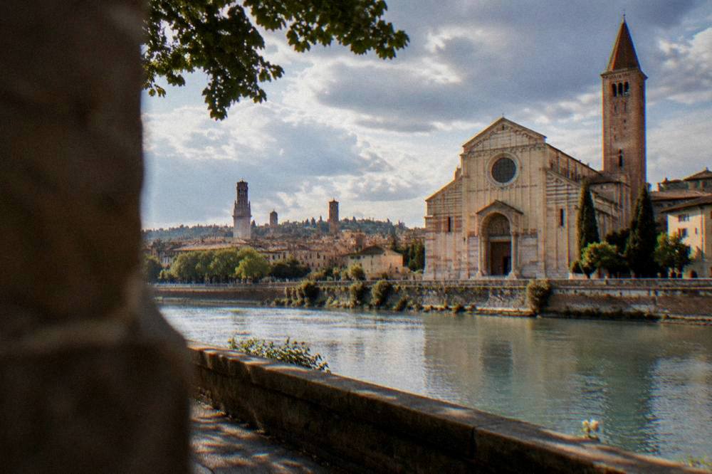 A view across the Adige river toward Verona's old rooftops and towers from a riverbank path