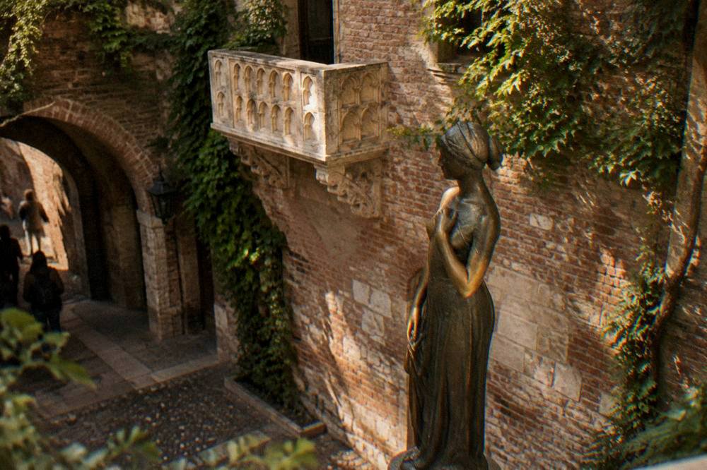 A bronze statue in a small courtyard photographed from below against a brick wall