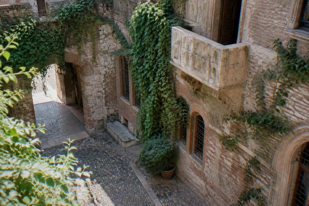 Narrow medieval courtyard with a stone balcony above and ivy on the walls, no people in focus