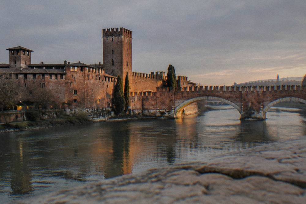 Castle walls and tower above the river at dusk with warm light on the brick