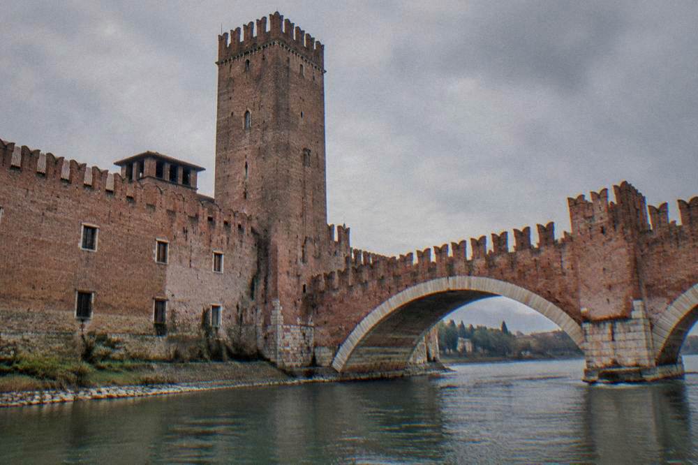 Brick castle walls and crenellations beside a river bridge