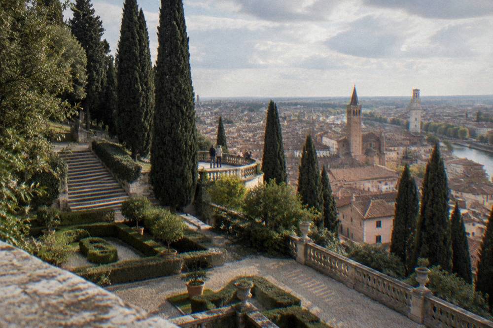 A stone belvedere terrace above red rooftops and church towers of a northern Italian city