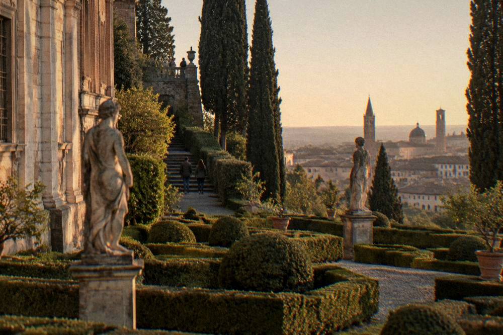 A formal garden parterre with clipped hedges and statuary beside a historic palace wall