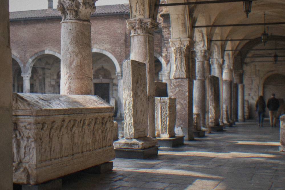 A stone sarcophagus and inscribed slabs standing in an open-air museum arcade