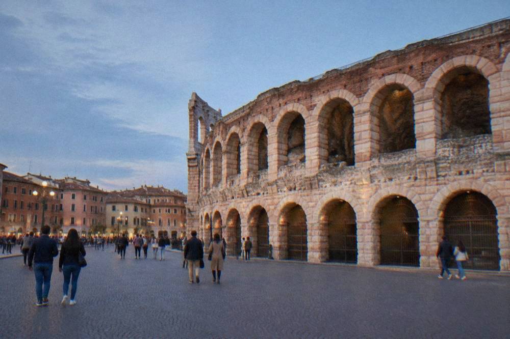 Visitors strolling the wide promenade of Piazza Bra with the Arena wall rising behind