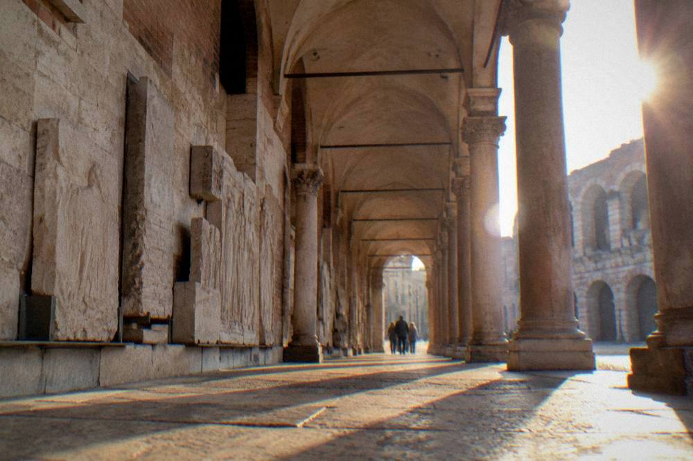 A quiet colonnade walkway with stone slabs set into the wall and daylight from the piazza