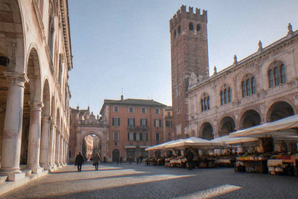 A cobbled square lined with historic buildings, market stalls and a stone tower under a clear sky