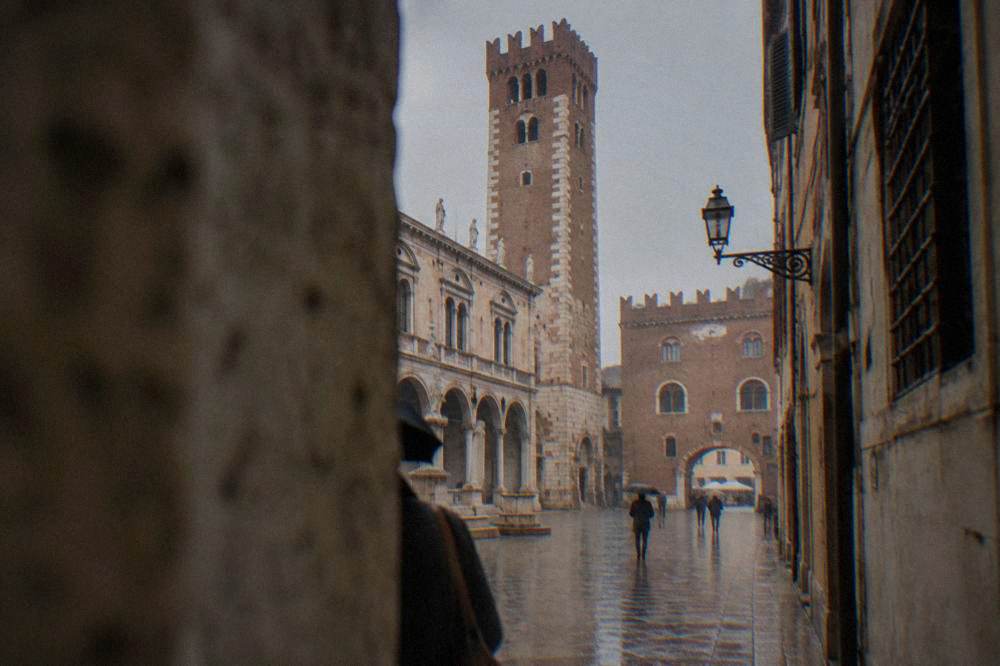 A tall medieval brick and stone tower seen from a narrow street between old buildings