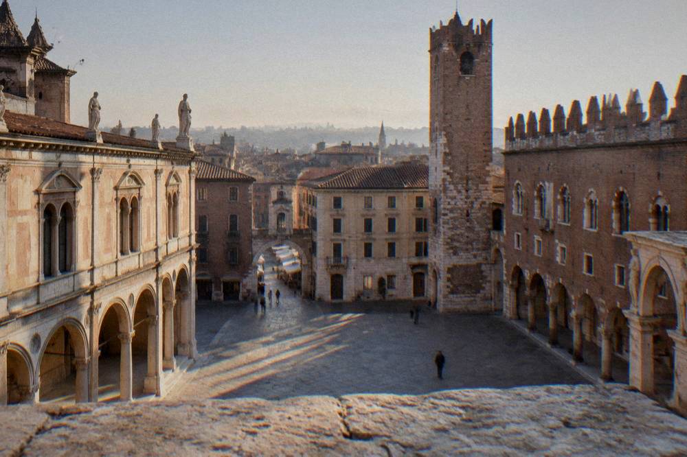 A stone city tower rising over red rooftops seen from a raised viewpoint in a historic city