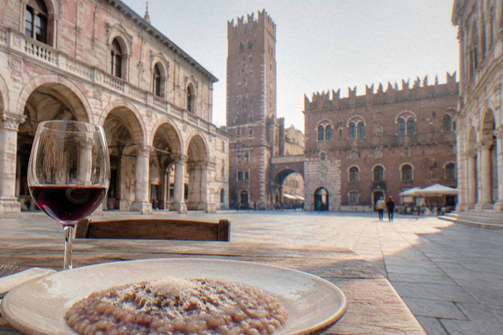 A plate of creamy risotto with red wine and a glass of local red wine on a rustic wooden table