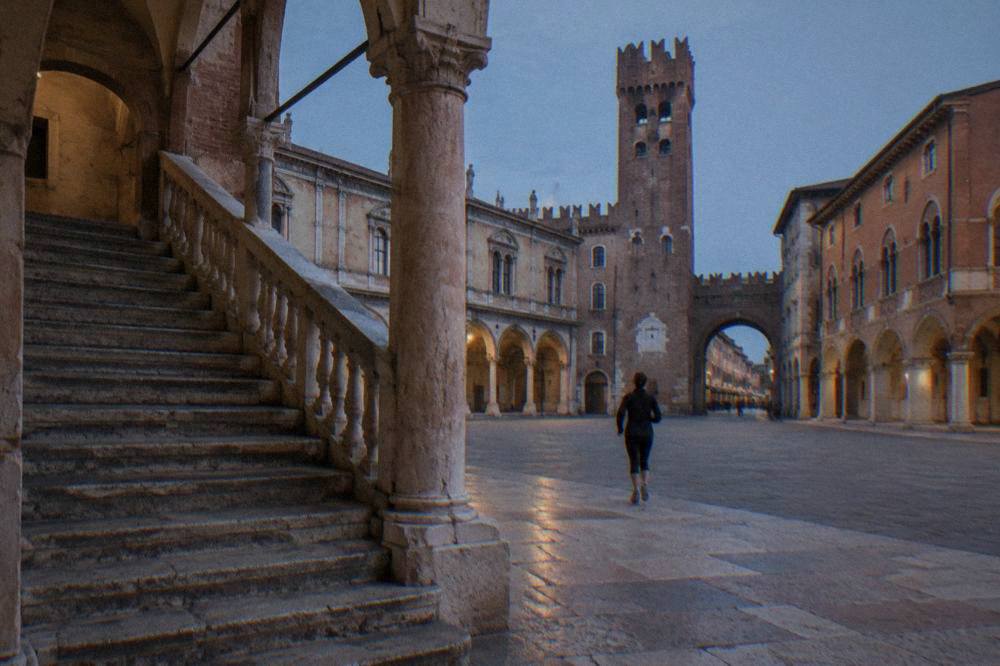 An old stone double staircase with worn steps framed by arches in a historic courtyard