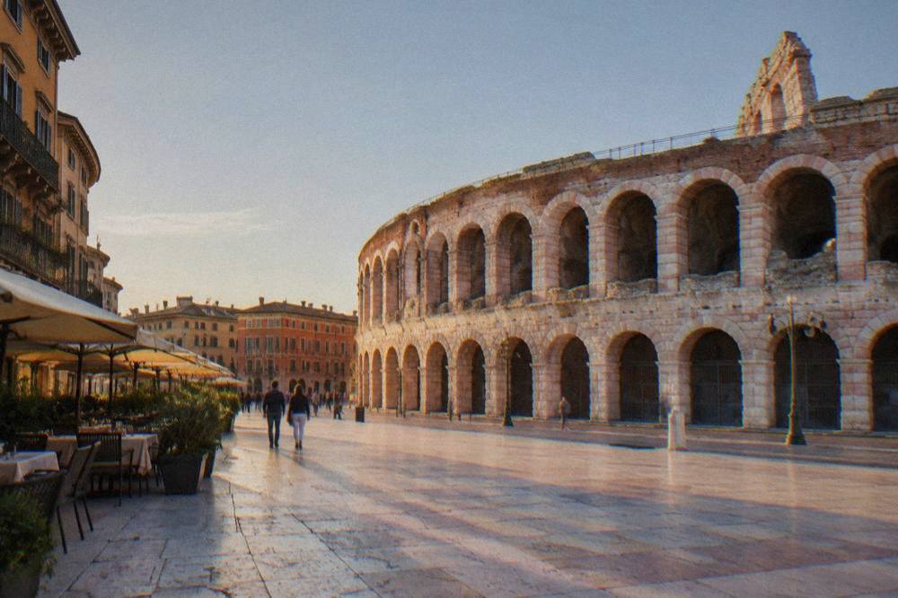 Evening light on the marble paving of the Liston promenade with cafe tables and the curved Arena wall in the background